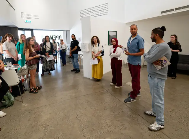 A group gathers in a white gallery space to listen to a talk.
